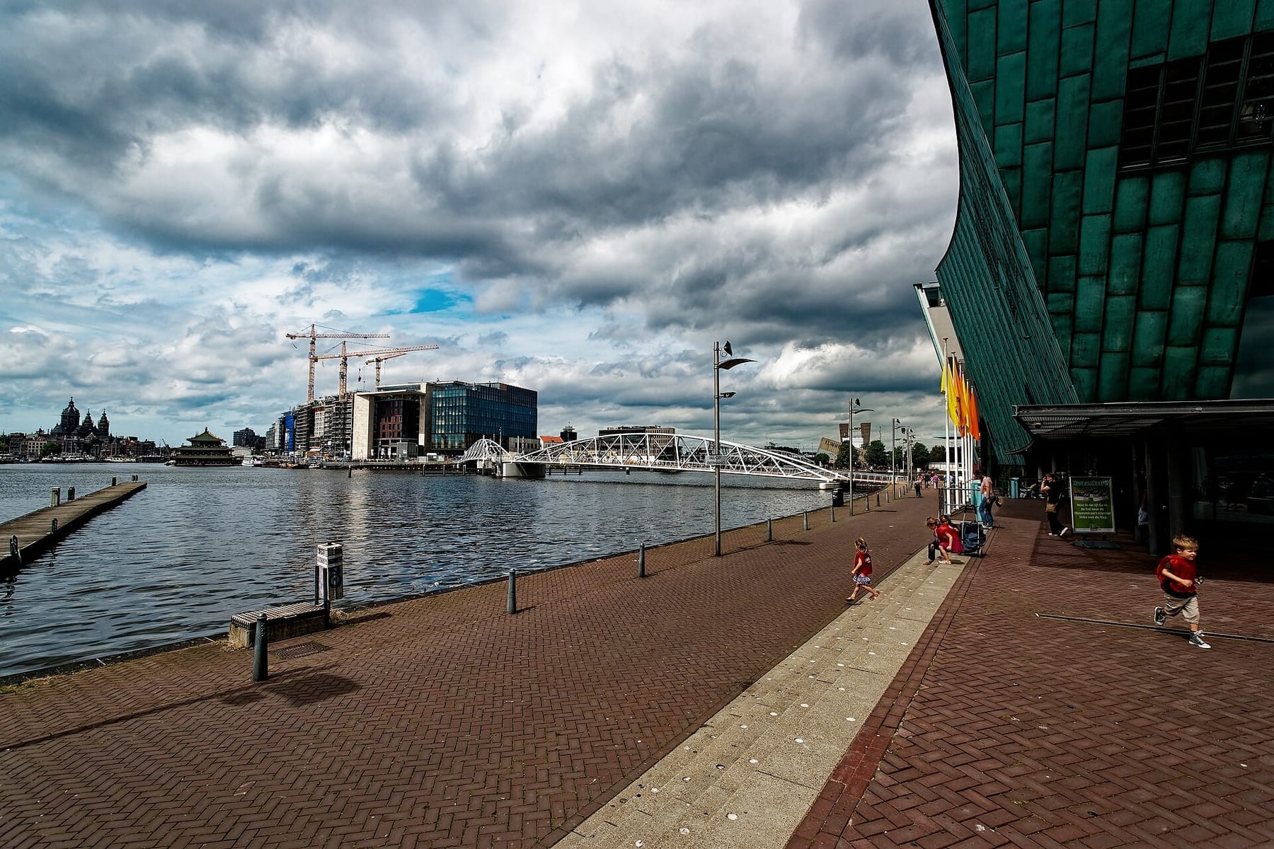 Amsterdam - Oosterdok - NEMO Science Centre 1997 by Renzo Piano - View NNW towards Amsterdam Public Library, Conservatory Amsterdam & Brug 1939, Mr. J.J. van der Velde brug (photograph from the Wikimedia Commons category Conservatorium van Amsterdam)